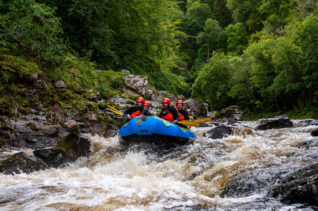 A group of white water rafters in a boat going down rapids on a river