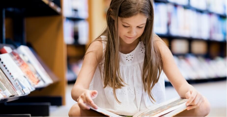 A child sitting on the floor of a library reading a book
