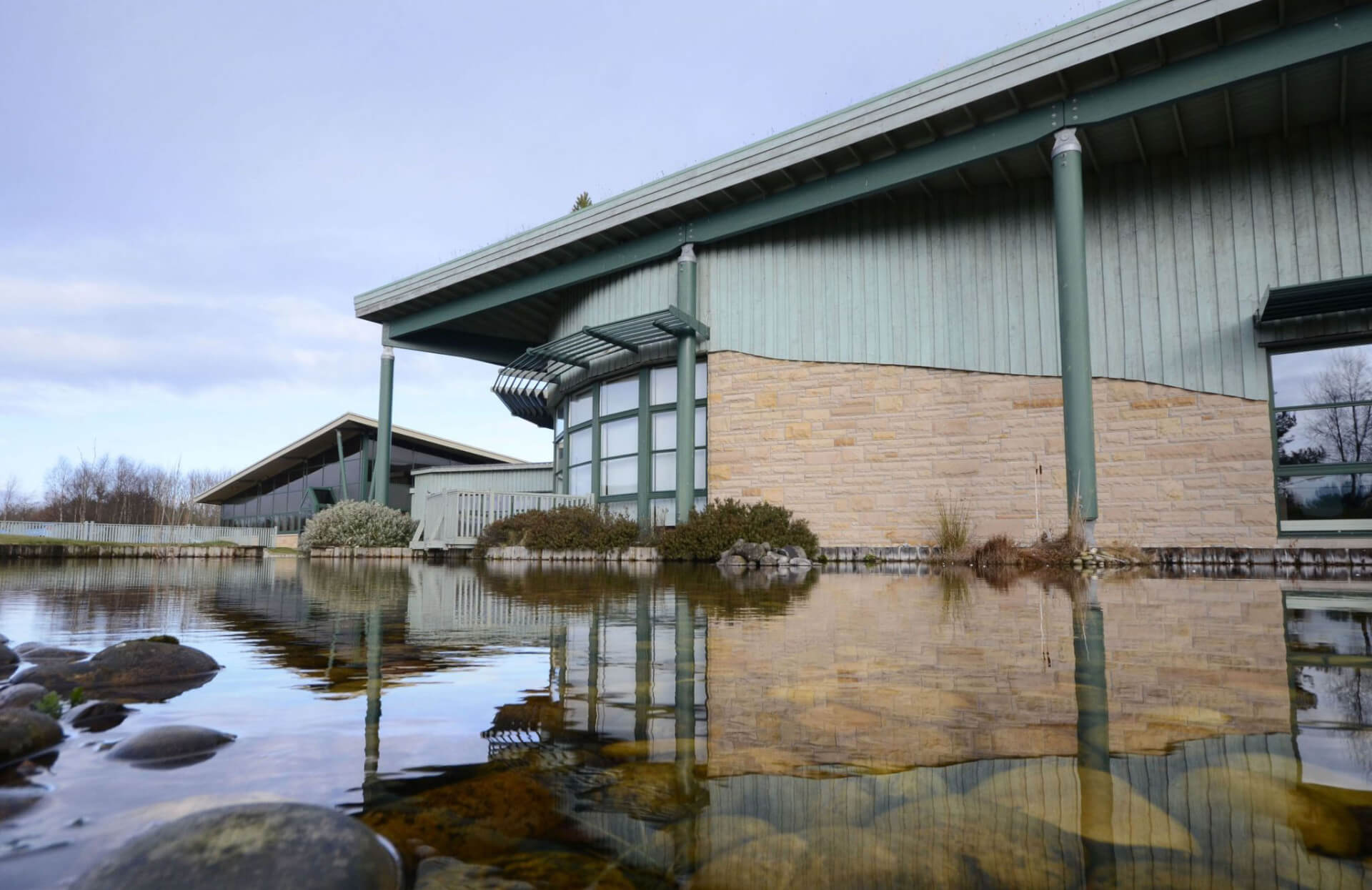 A photo of the Horizon building in Moray surrounded by a pond, the reflection of the building can be seen in the still water